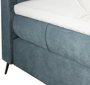 Nahaufnahme eines Boxspringbetts 180x200 mit grauem Stoffbezug und weißer Matratze, seitliche Perspektive