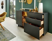 Modernes Sideboard mit offenen Schubladen, seitliche Perspektive, dekoriert mit Geschirr und einer Vase, vor einer grünen Wand.