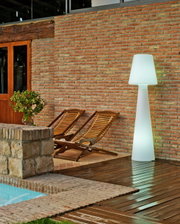 LED-buitenstaande lamp Lola 165, verlicht, op een terras naast twee houten ligstoelen en een bakstenen muur, zijaanzicht
