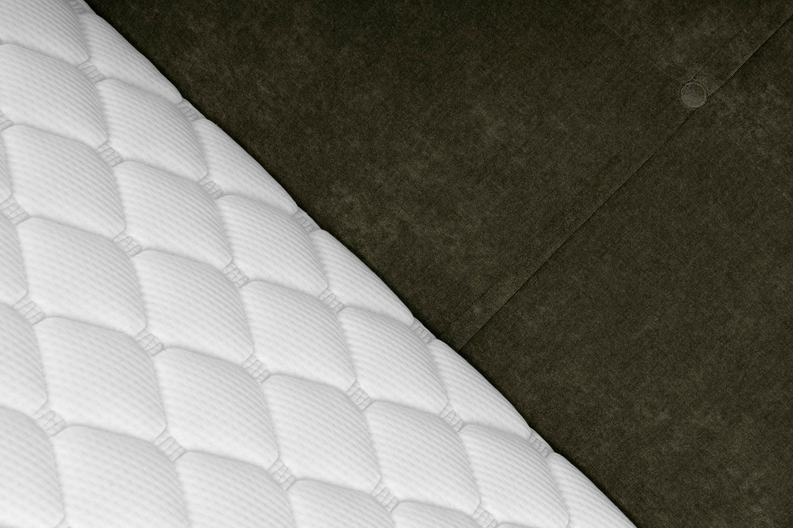 Nahaufnahme eines Boxbetts mit weißer, gesteppten Matratze und dunkelgrauem, gepolstertem Kopfteil, diagonale Perspektive