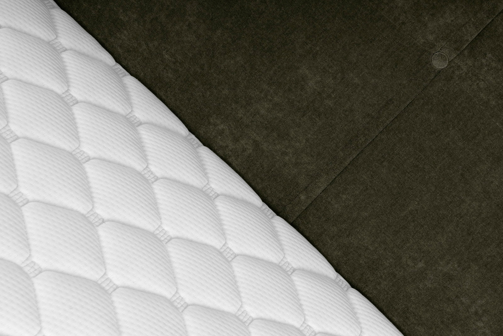 Nahaufnahme eines Boxbetts mit weißer, gesteppten Matratze und dunkelgrauem, gepolstertem Kopfteil, diagonale Perspektive