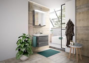Moderne Badezimmeransicht mit Waschtisch, Spiegel und Badewanne im Hintergrund, aus der Perspektive von links vorne.