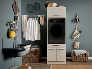Modern eingerichteter Hauswirtschaftsraum mit schwarzer Frontlader-Waschmaschine im weißen Schrank, daneben Waschbecken, Wäsche auf Stange und Körbe; Frontalansicht auf das Produkt.