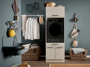 Modern eingerichteter Hauswirtschaftsraum mit schwarzer Frontlader-Waschmaschine im weißen Schrank, daneben Waschbecken, Wäsche auf Stange und Körbe; Frontalansicht auf das Produkt.