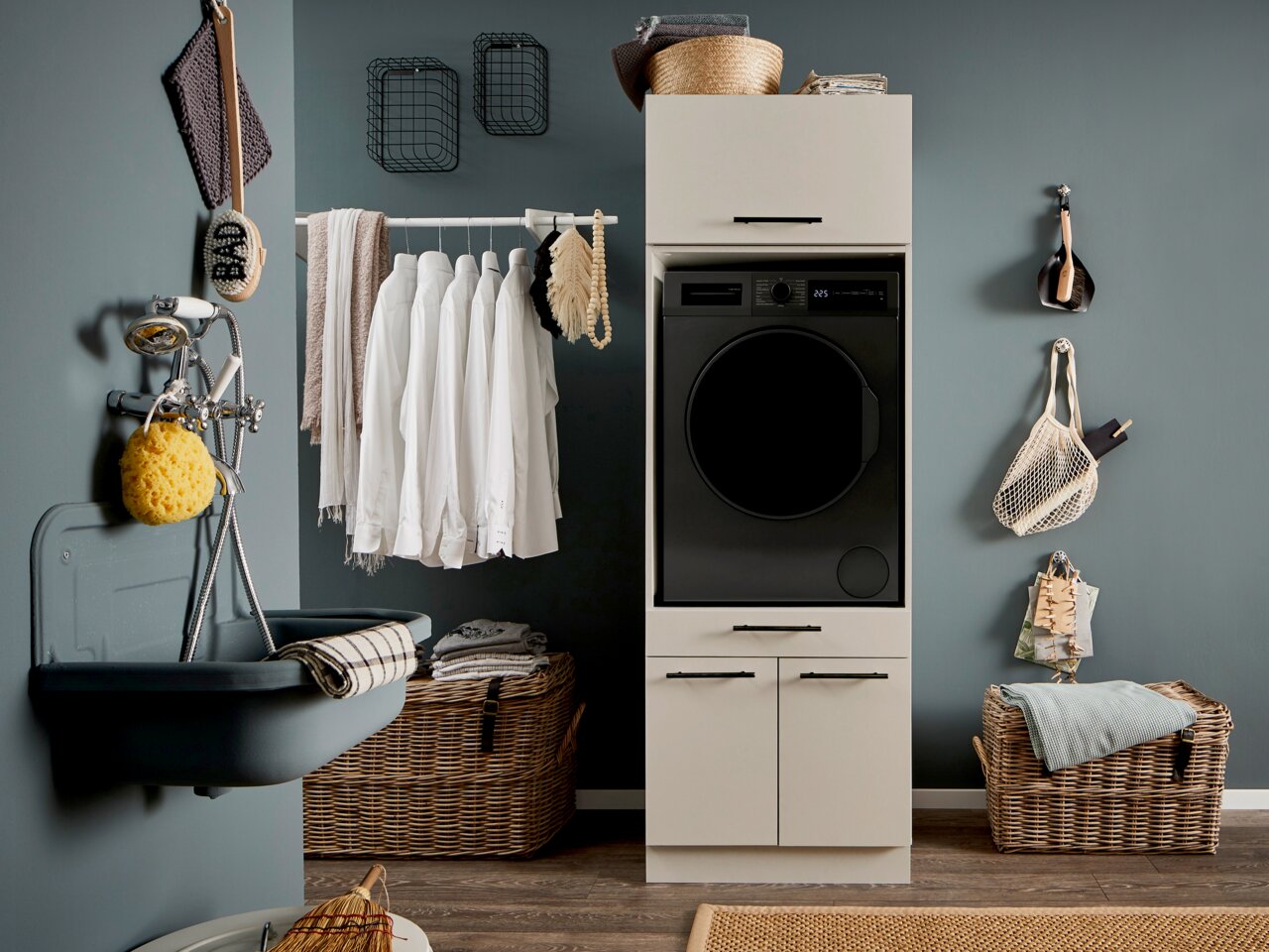 XORA Hauswirtschaftsraum-Kombi PRIMUS Modern eingerichteter Hauswirtschaftsraum mit schwarzer Frontlader-Waschmaschine im weißen Schrank, daneben Waschbecken, Wäsche auf Stange und Körbe; Frontalansicht auf das Produkt.