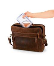 Eine Hand legt eine Frischhaltedose in eine braune Ledertasche, seitliche Perspektive.