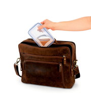 Eine Hand legt eine Frischhaltedose in eine braune Ledertasche, seitliche Perspektive.