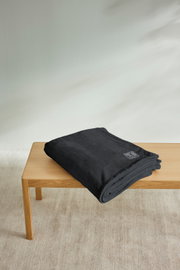 Gefaltete schwarze Kuscheldecke von s.Oliver auf einem Holztisch, seitliche Perspektive.