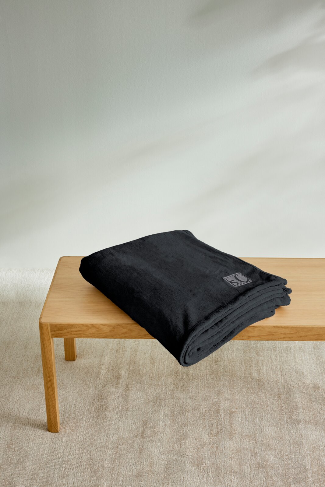 Gefaltete schwarze Kuscheldecke von s.Oliver auf einem Holztisch, seitliche Perspektive.