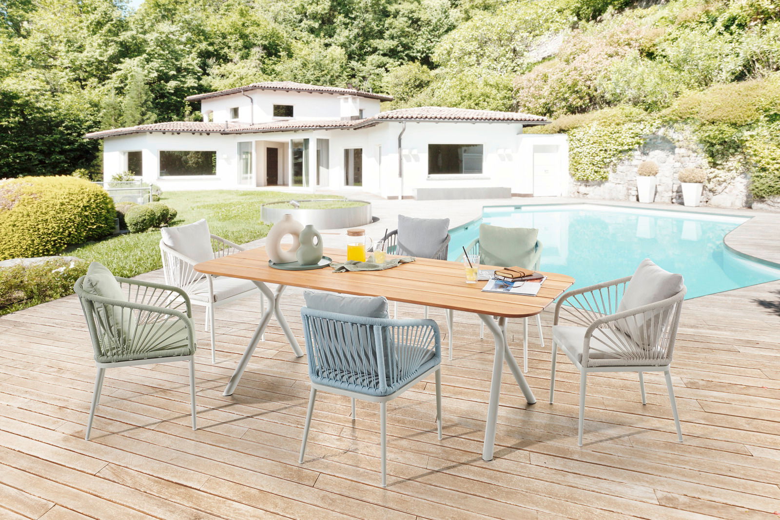 Niehoff-Garden Sessel IZOLA Gartenmöbel-Set mit modernen Sesseln und Holztisch auf einer Terrasse mit Pool, im Hintergrund ein weißes Haus und grüne Landschaft, Perspektive von schräg oben.
