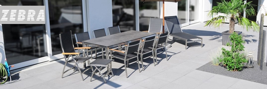Een modern terras met een grote tuintafel, zwarte stoelen, een ligstoel en een palmboom.