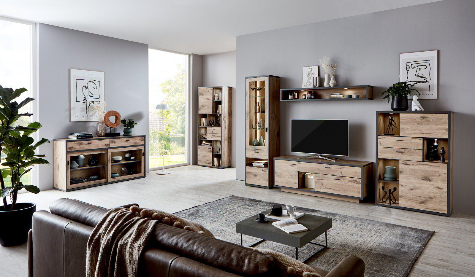 Wohnzimmeransicht mit moderner Wandkombination ORLANDO von Zurbrüggen in Holzoptik, bestehend aus Vitrine, Sideboard, Wandregal und TV-Element, mit Dekorationen und Pflanzen, seitliche Perspektive.