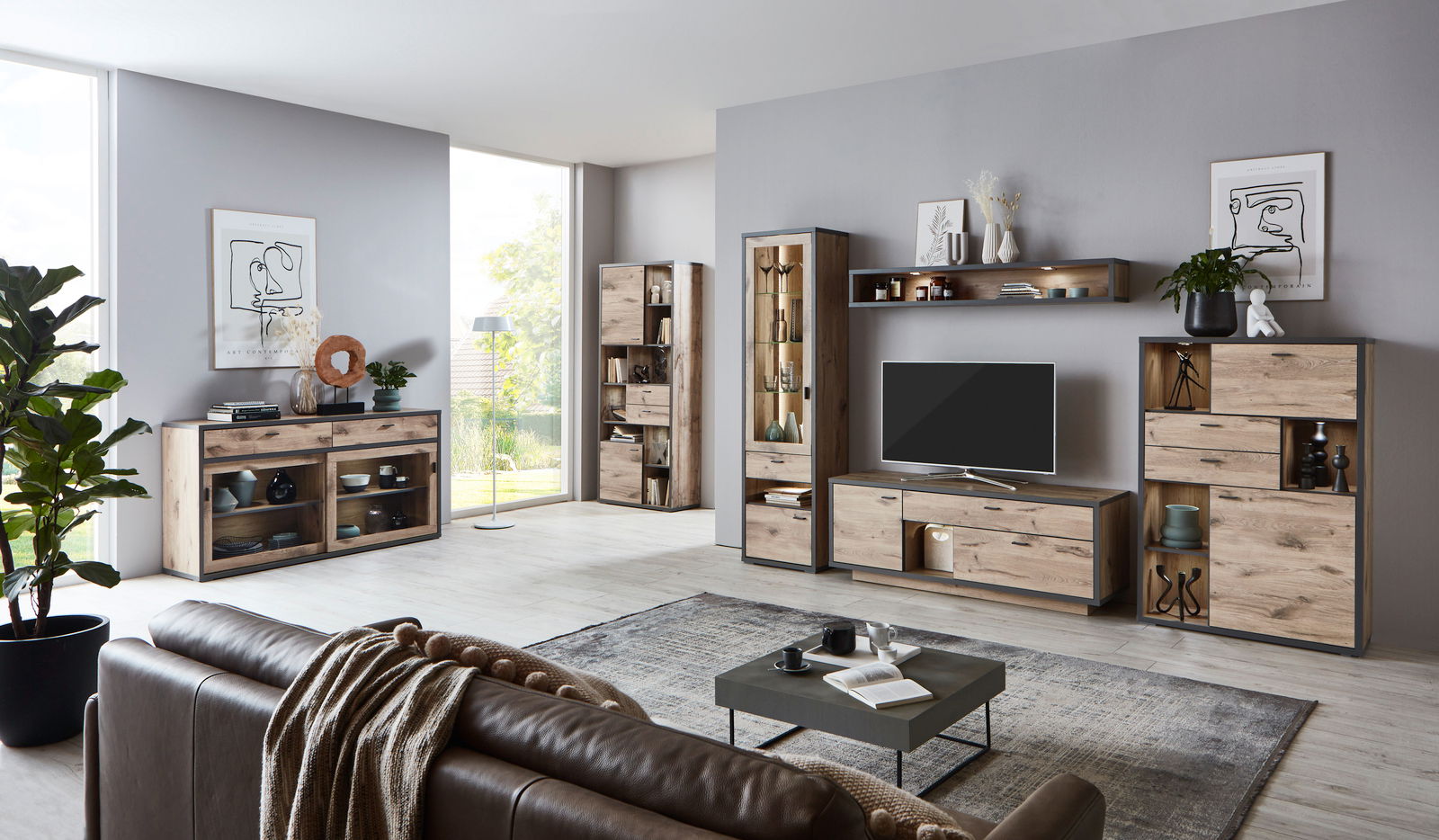 Wohnzimmeransicht mit moderner Wandkombination ORLANDO von Zurbrüggen in Holzoptik, bestehend aus Vitrine, Sideboard, Wandregal und TV-Element, mit Dekorationen und Pflanzen, seitliche Perspektive.