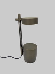 Moderne Tischlampe in Dunkelgrau mit zylindrischem Fuß und rundem Lampenkopf, seitliche Ansicht in leichter Perspektive von vorne, mit sichtbarem Kabel vor hellem Hintergrund