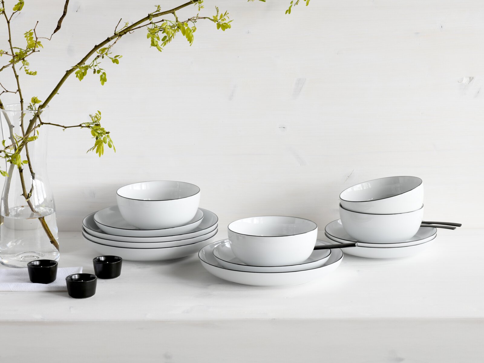 Creatable Tellerset 12-tlg ALLROUND Minimalistisches weißes Geschirrset mit Schalen und Tellern mit feinem dunklem Rand, seitliche Frontansicht auf einem hellen Tisch, links Glasvase mit Zweig