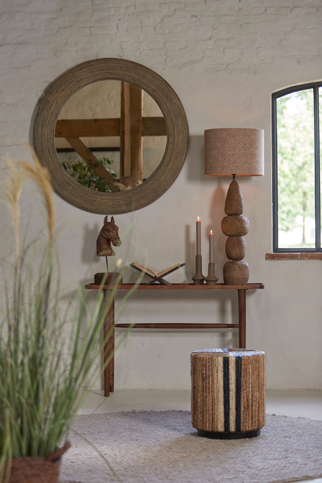 Ein stilvoller Raum mit einem runden Spiegel, einer Tischlampe mit einem natürlichen Steinsockel und einem braunen Lampenschirm. Die Perspektive zeigt die Lampe von der Seite.