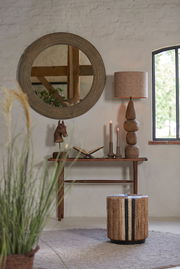 Ein stilvoller Raum mit einem runden Spiegel, einer Tischlampe mit einem natürlichen Steinsockel und einem braunen Lampenschirm. Die Perspektive zeigt die Lampe von der Seite.
