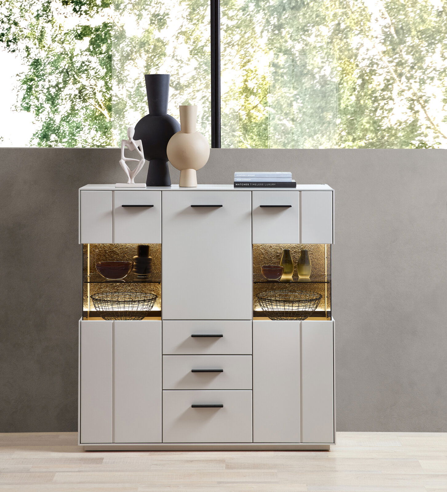 Zurbrüggen Highboard COMO Modernes Highboard in Weiß mit schwarzen Griffen, dekoriert mit Vasen und Büchern, frontal fotografiert.