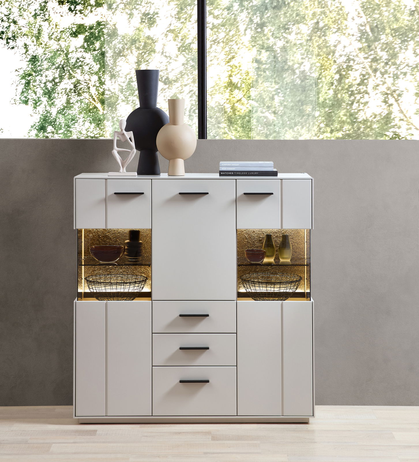 Modernes Highboard in Weiß mit schwarzen Griffen, dekoriert mit Vasen und Büchern, frontal fotografiert.