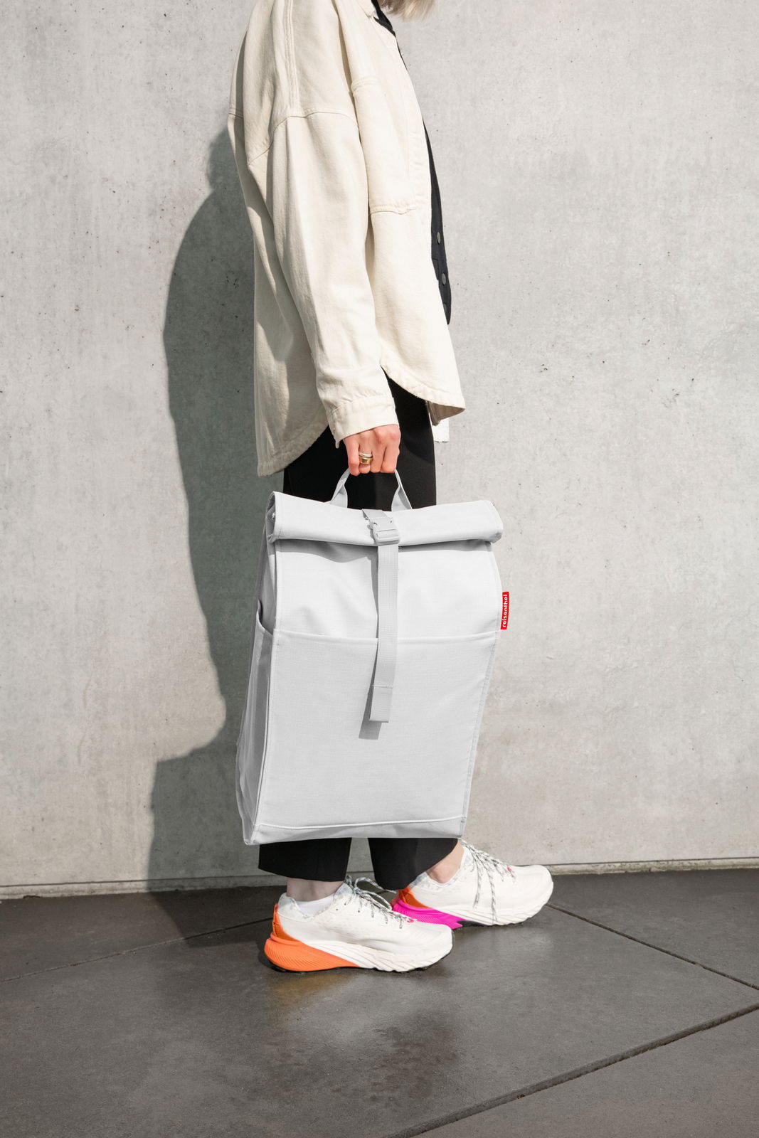 Person trägt einen grauen Rolltop-Rucksack in der Hand, seitliche Perspektive.