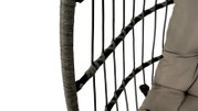 Close-up van een hangstoel met gevlochten frame en een beige kussen, gezien vanaf de zijkant