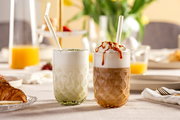 Zwei Gläser mit Matcha Latte und Karamell Latte auf einem gedeckten Tisch, seitliche Perspektive.