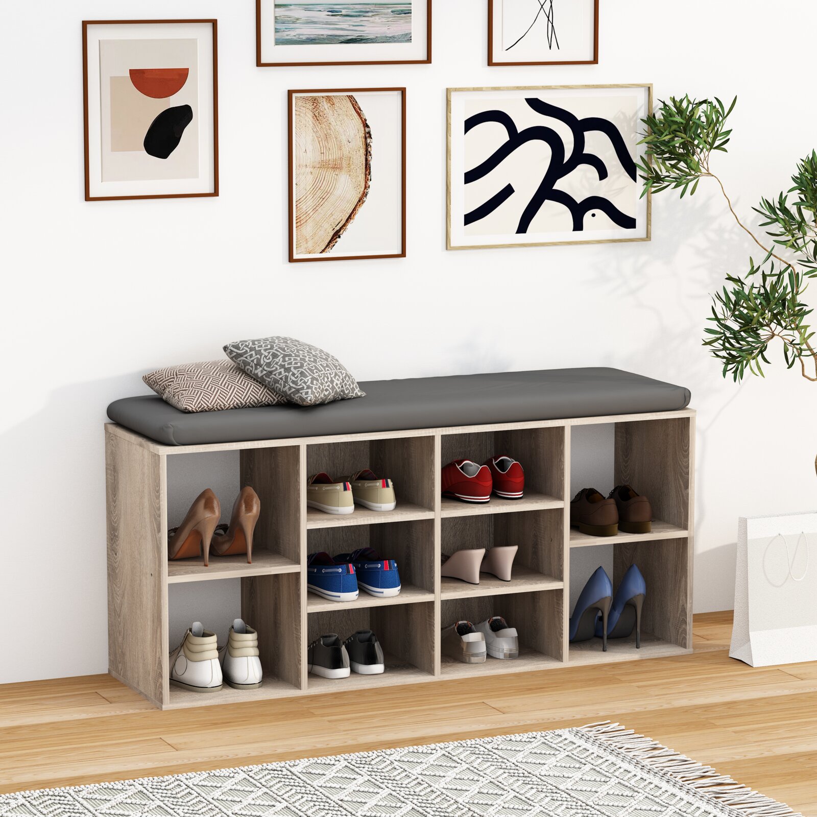 Schuhregal mit Sitzbank in heller Holzoptik und grauem Sitzpolster, mehrere offene Fächer mit Schuhen und Kissen, frontale Perspektive im Wohnraum.