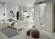 Modernes Schlafzimmer mit weißem Bettgestell, Nachttisch und Kleiderschrank, aus der Perspektive von vorne links aufgenommen.
