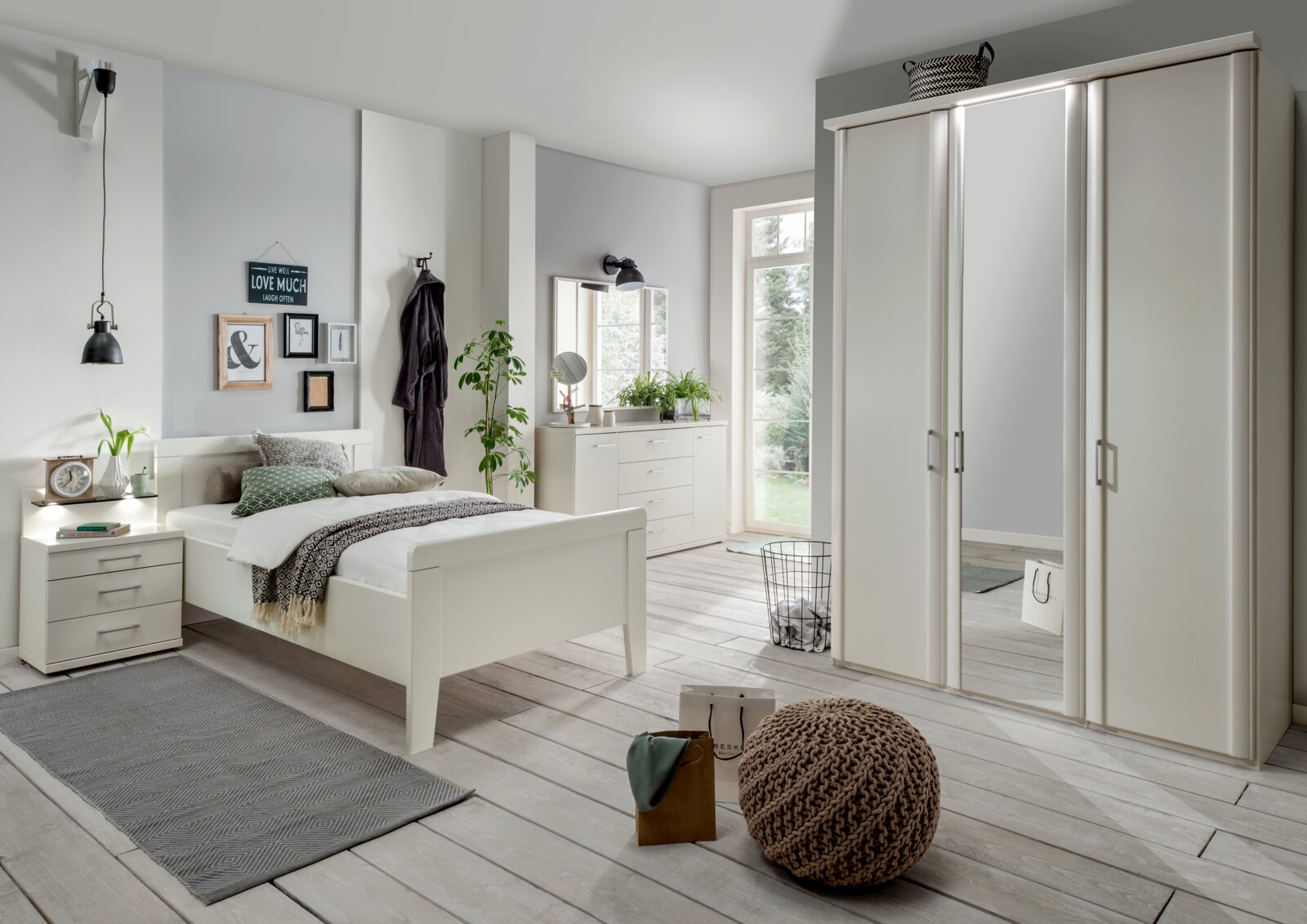 Modernes Schlafzimmer mit weißem Bettgestell, Nachttisch und Kleiderschrank, aus der Perspektive von vorne links aufgenommen.