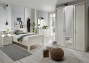 Modernes Schlafzimmer mit weißem Bettgestell, Nachttisch und Kleiderschrank, aus der Perspektive von vorne links aufgenommen.