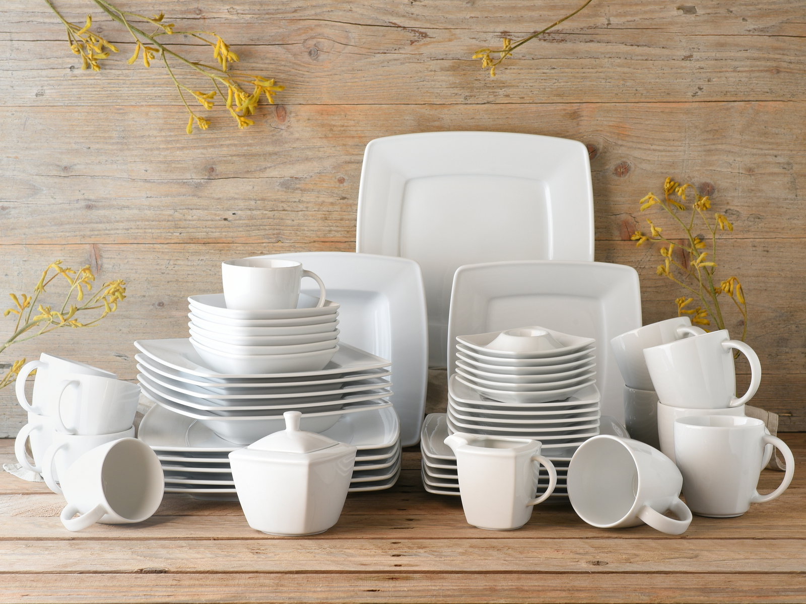 Creatable Kombiservice 50-tlg VICTORIA Kombiservice 50-tlg in moderner, quadratischer Form, bestehend aus Tellern, Tassen und Schalen, auf einem Holztisch arrangiert, frontal fotografiert.