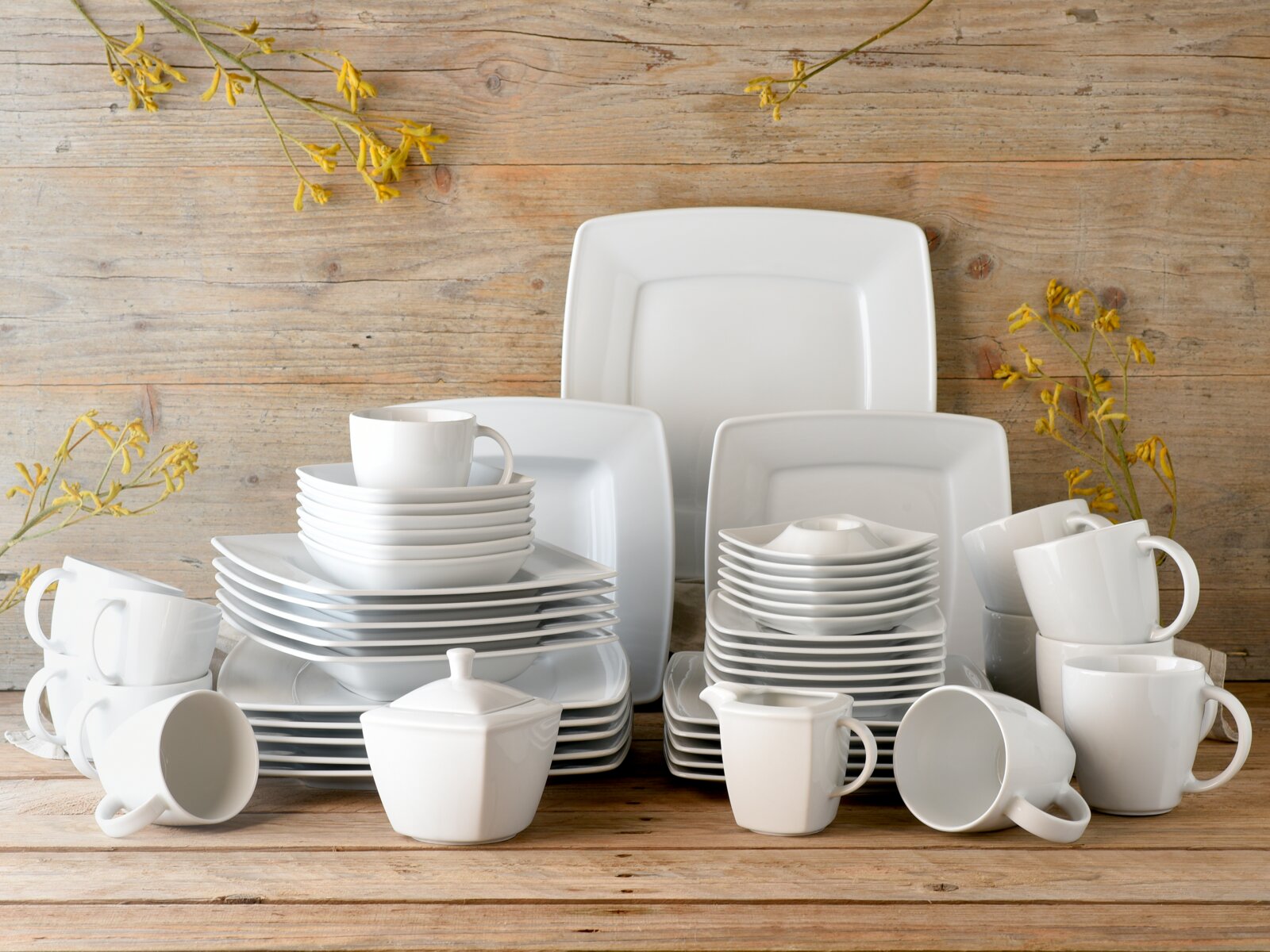 Creatable Kombiservice 50-tlg VICTORIA Kombiservice 50-tlg in moderner, quadratischer Form, bestehend aus Tellern, Tassen und Schalen, auf einem Holztisch arrangiert, frontal fotografiert.
