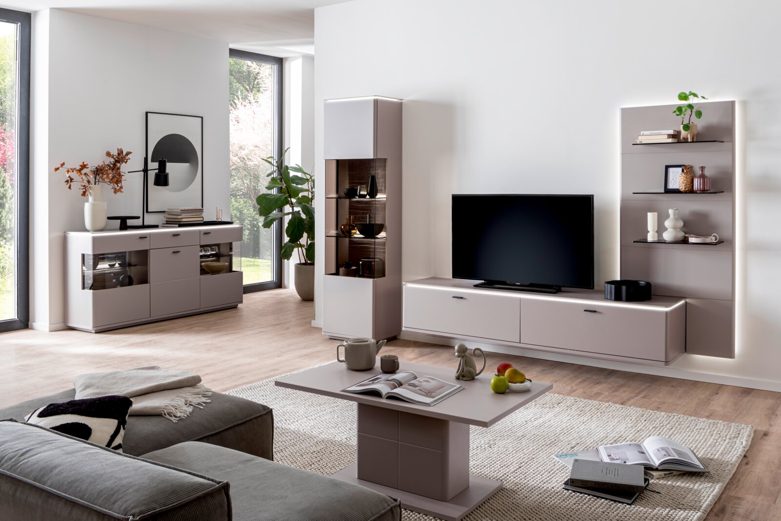 Zurbrüggen Wandkombination TORRENT Modernes Wohnzimmer mit taupefarbenem Wohnwand-Set: Lowboard mit Fernseher, Vitrine, Sideboard und Wandregal mit LED-Beleuchtung, aufgenommen aus leicht schräger Frontperspektive auf Augenhöhe.