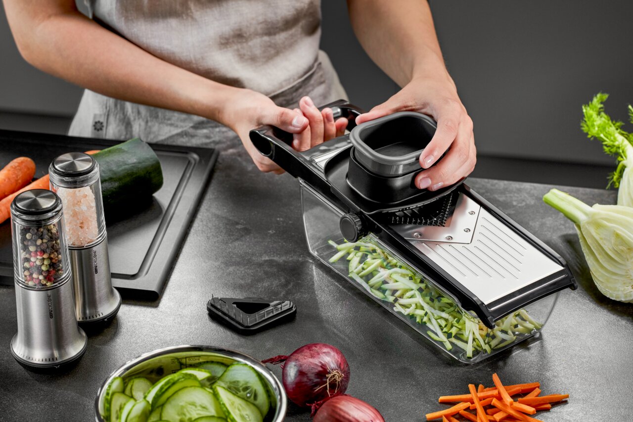 V-Hobel Julienne mit Auffangbehälter, seitliche Perspektive, während Gemüse in feine Streifen geschnitten wird.