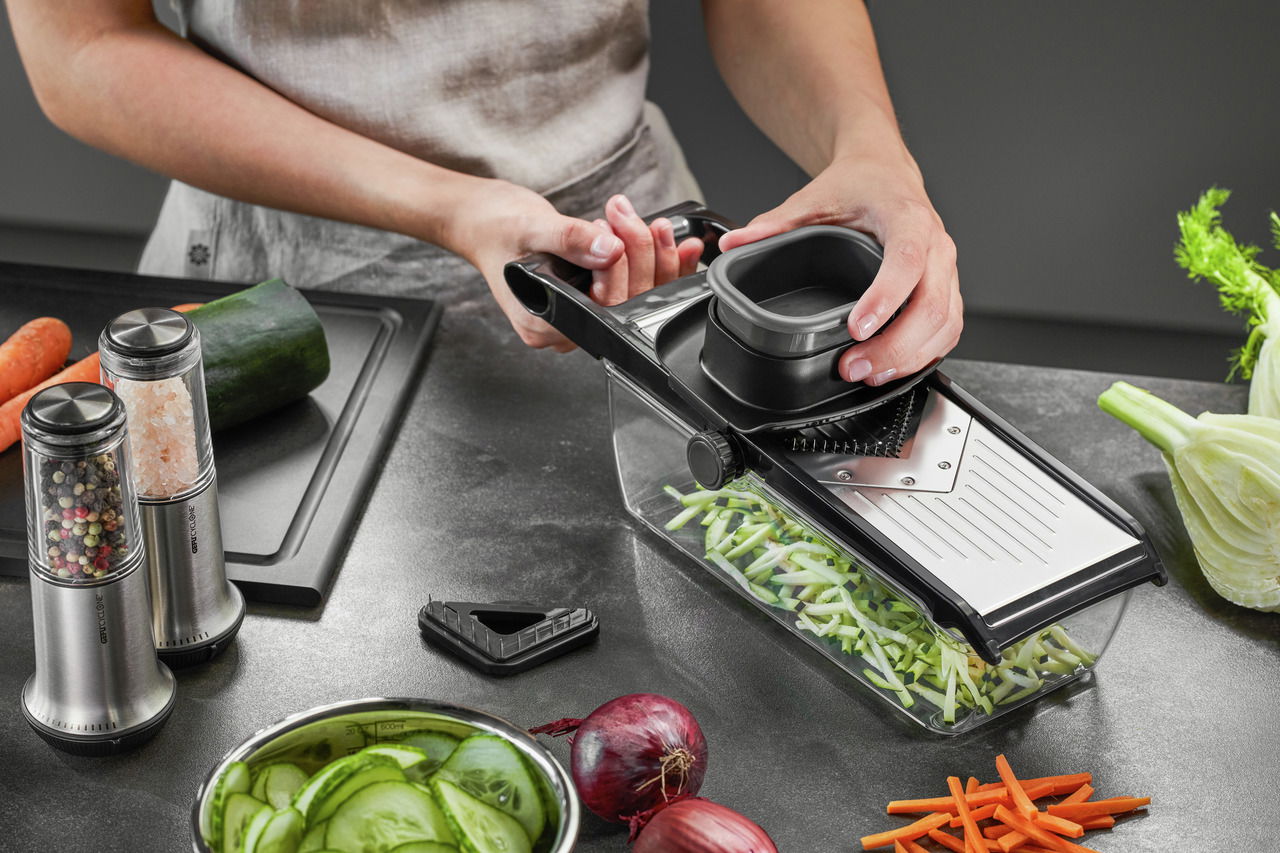 V-Hobel Julienne mit Auffangbehälter, seitliche Perspektive, während Gemüse in feine Streifen geschnitten wird.