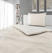 Bettwäsche-Set in Cremefarbe auf einem Bett, mit Kissen und Decke, in einem modernen Schlafzimmer mit Bücherregal und Dekorationen, seitliche Perspektive