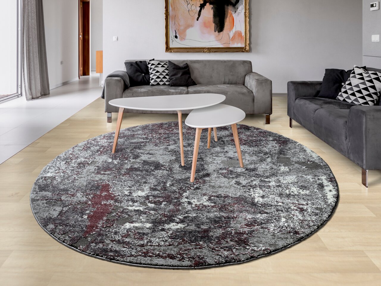 Runder Designer Teppich in einem modernen Wohnzimmer, mit grauen und roten Mustern, aus der Vogelperspektive betrachtet.
