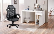 Schwarzer Gaming-Stuhl mit ergonomischem Design und gepolsterter Sitzfläche, seitliche Perspektive, neben einem weißen Schreibtisch in einem modernen Raum.