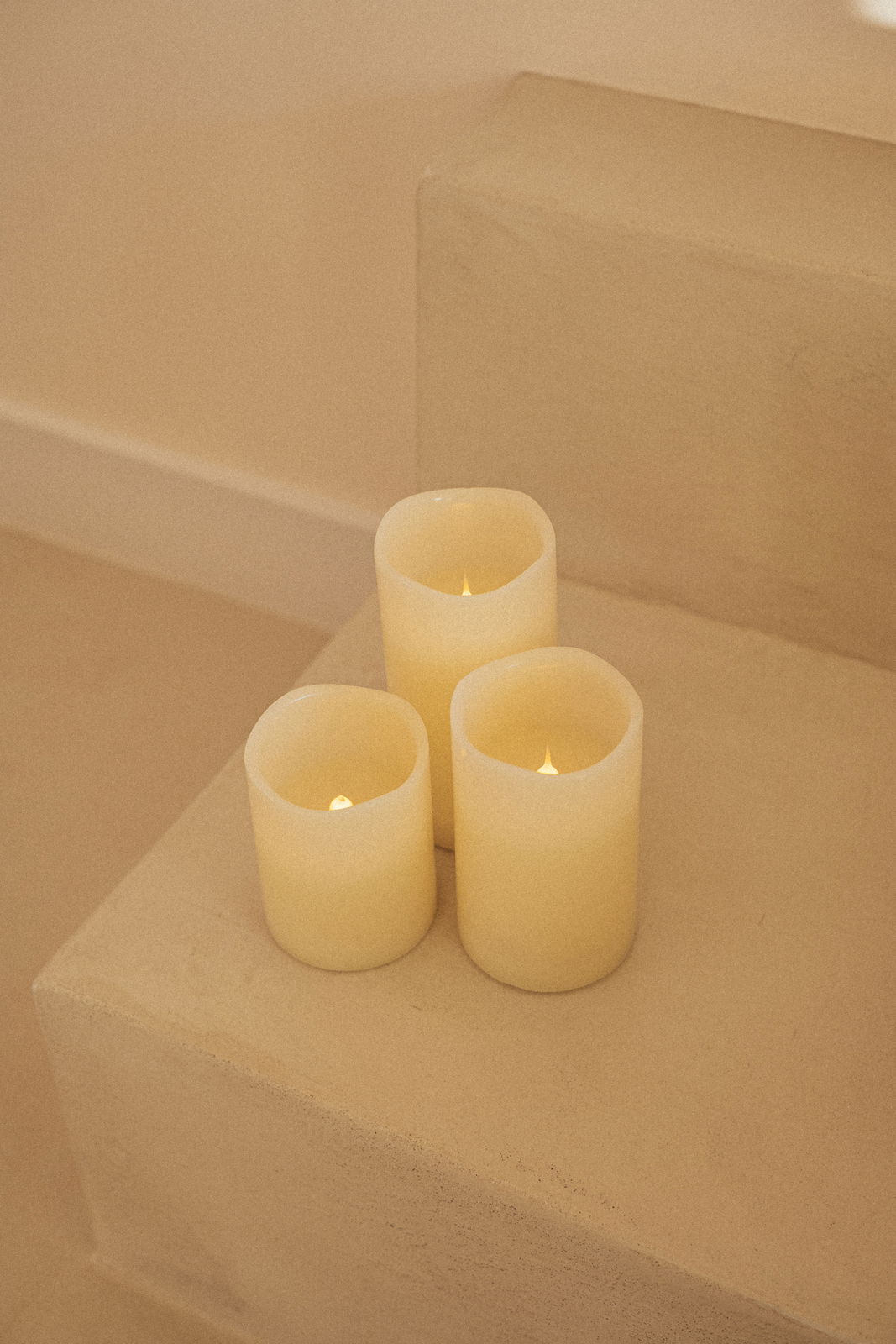 Drei cremefarbene Outdoor-Kerzen auf einer Treppe, von oben betrachtet.