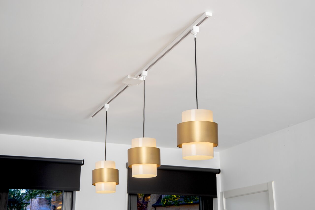 Pendelleuchten-Adapter in Weiß, montiert an einer Decke mit drei hängenden, goldfarbenen Lampenschirmen. Perspektive von unten.