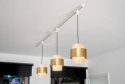Pendelleuchten-Adapter in Weiß, montiert an einer Decke mit drei hängenden, goldfarbenen Lampenschirmen. Perspektive von unten.