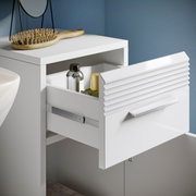 Weißer Standschrank mit geöffneter Schublade, seitliche Perspektive, zeigt Innenraum mit Flaschen und Bürste auf der Oberseite.
