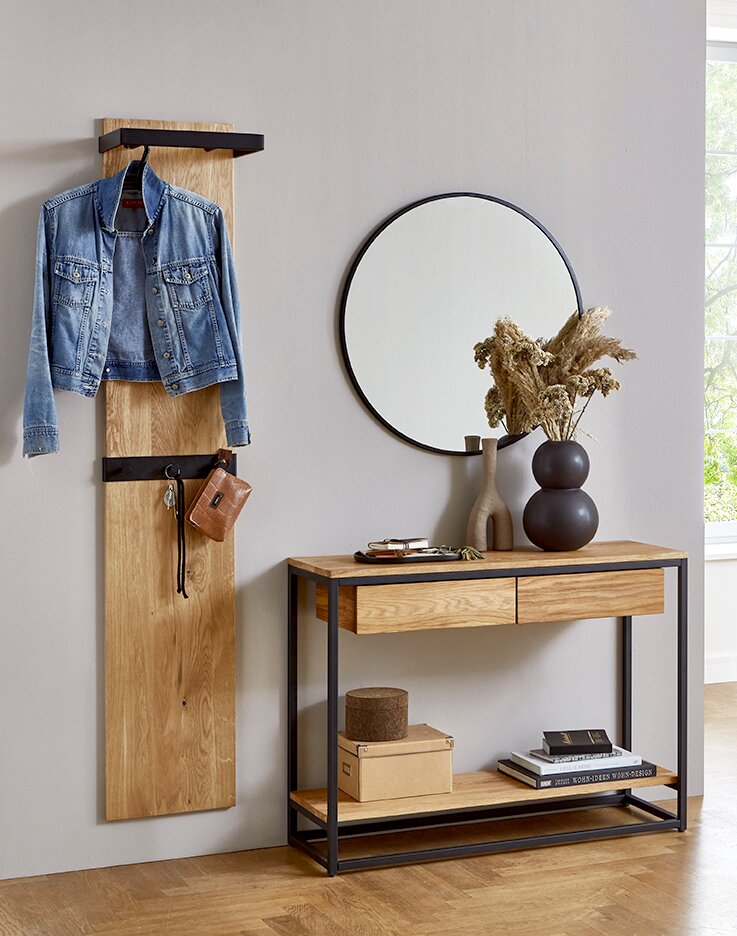 Frontalansicht eines modernen Flurs mit Wandgarderobe aus Holz und schwarzem Metallhaken, daneben Konsole aus Holz mit schwarzem Metallgestell, rundem Spiegel und dekorativen Vasen.