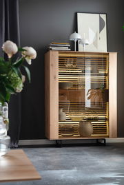 Modernes Highboard aus Holz mit Glastüren, dekoriert mit Büchern und Lampen, seitliche Perspektive