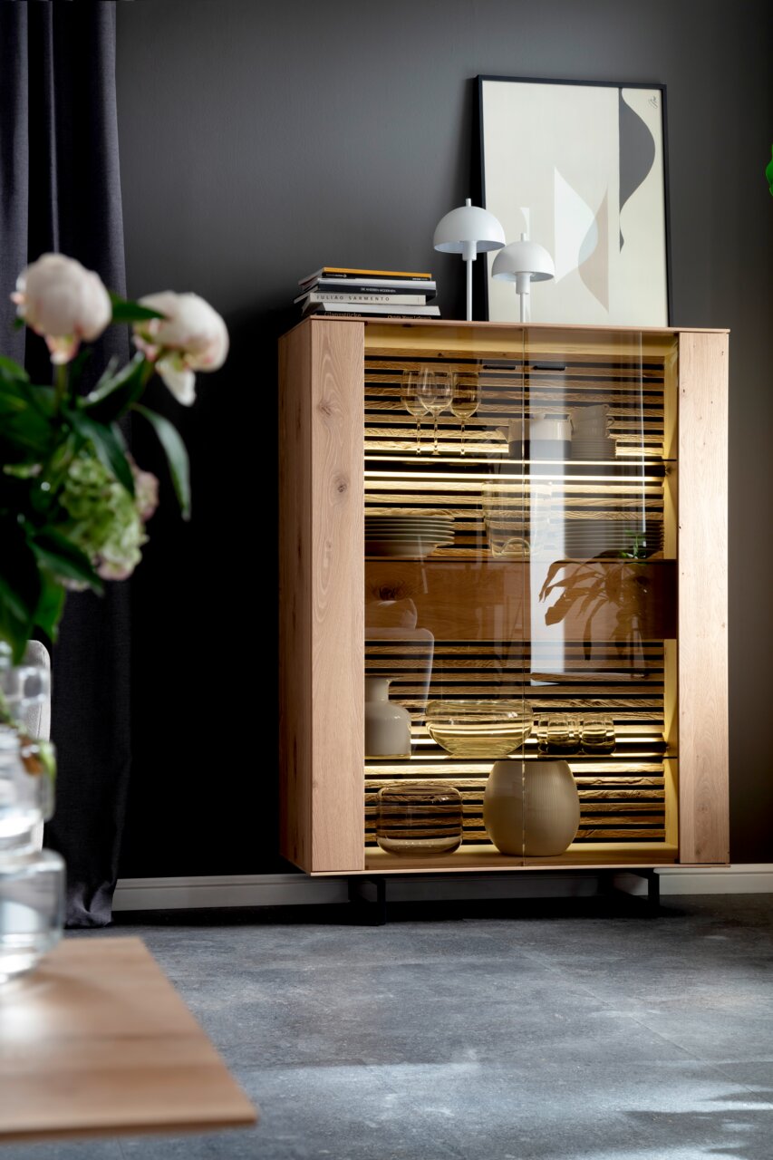 Modern houten hoogkast met glazen deuren, versierd met boeken en lampen, zijaanzicht
