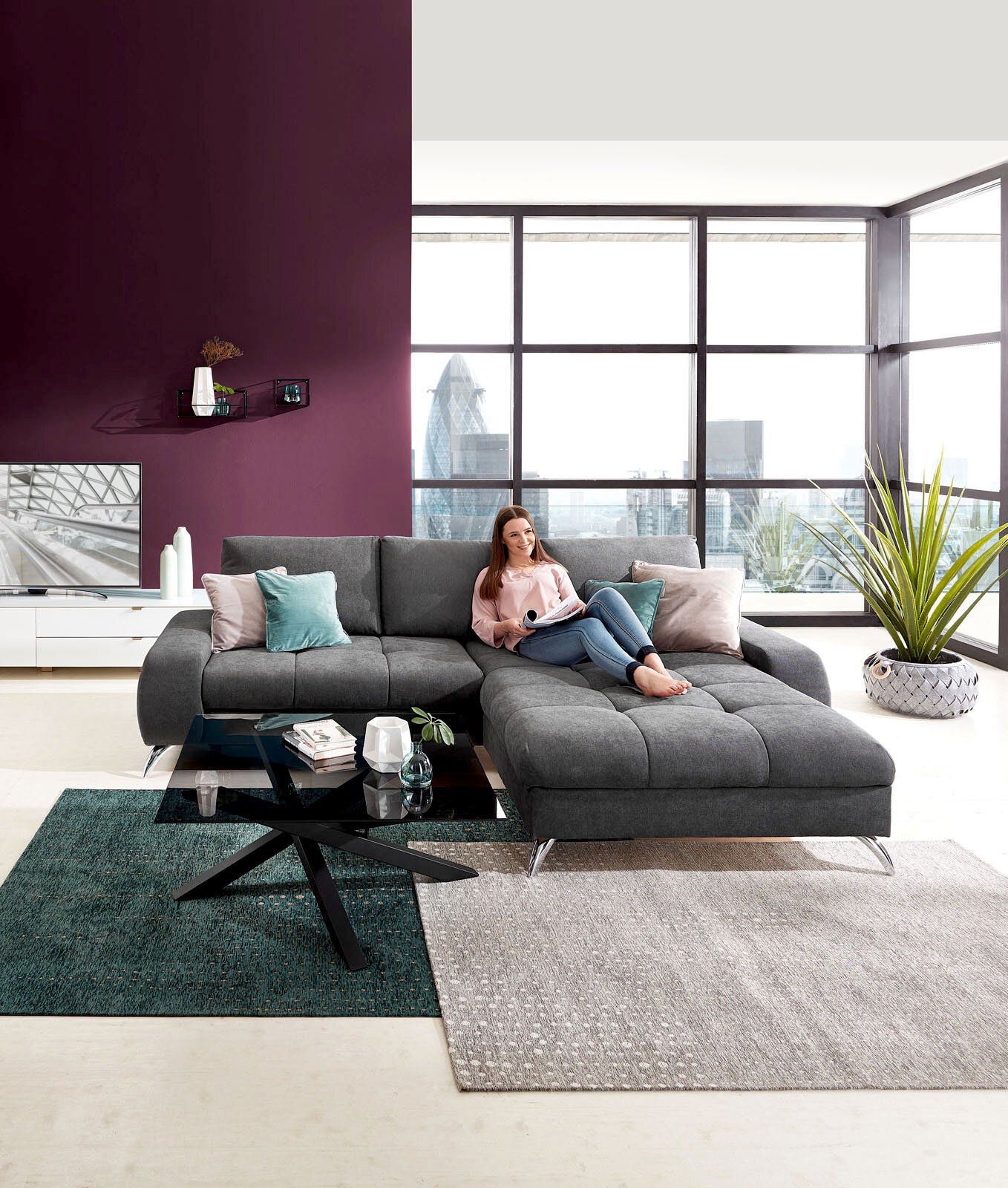 Moderner Couchtisch mit schwarzer Glasplatte und gekreuztem Metallgestell, im Vordergrund einer stilvollen Wohnzimmerumgebung mit grauem Ecksofa. Perspektive: Frontalansicht.