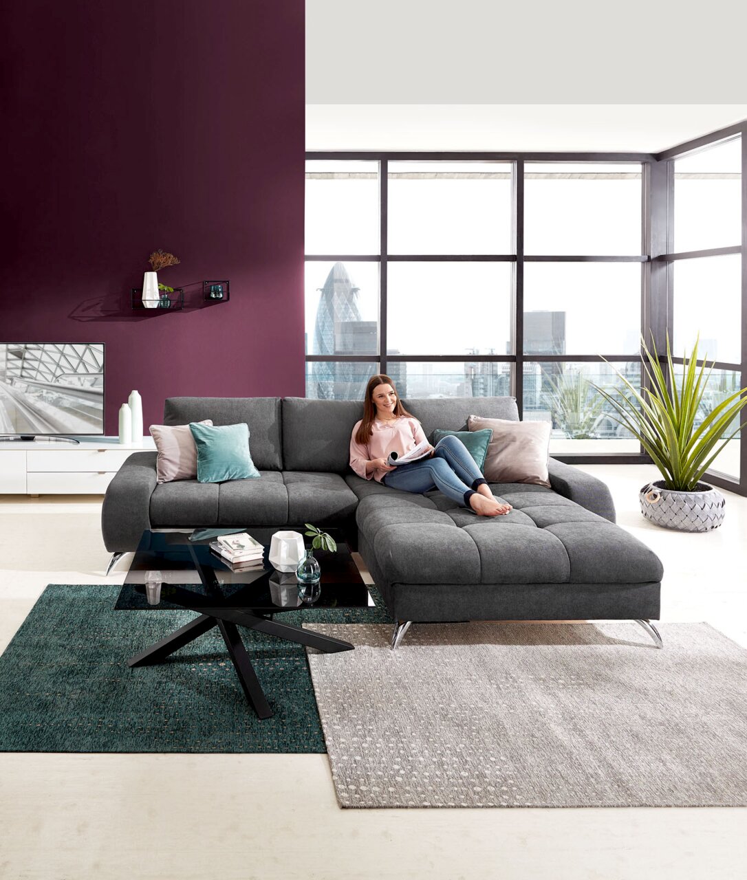 Moderner Couchtisch mit schwarzer Glasplatte und gekreuztem Metallgestell, im Vordergrund einer stilvollen Wohnzimmerumgebung mit grauem Ecksofa. Perspektive: Frontalansicht.