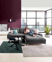 Moderner Couchtisch mit schwarzer Glasplatte und gekreuztem Metallgestell, im Vordergrund einer stilvollen Wohnzimmerumgebung mit grauem Ecksofa. Perspektive: Frontalansicht.