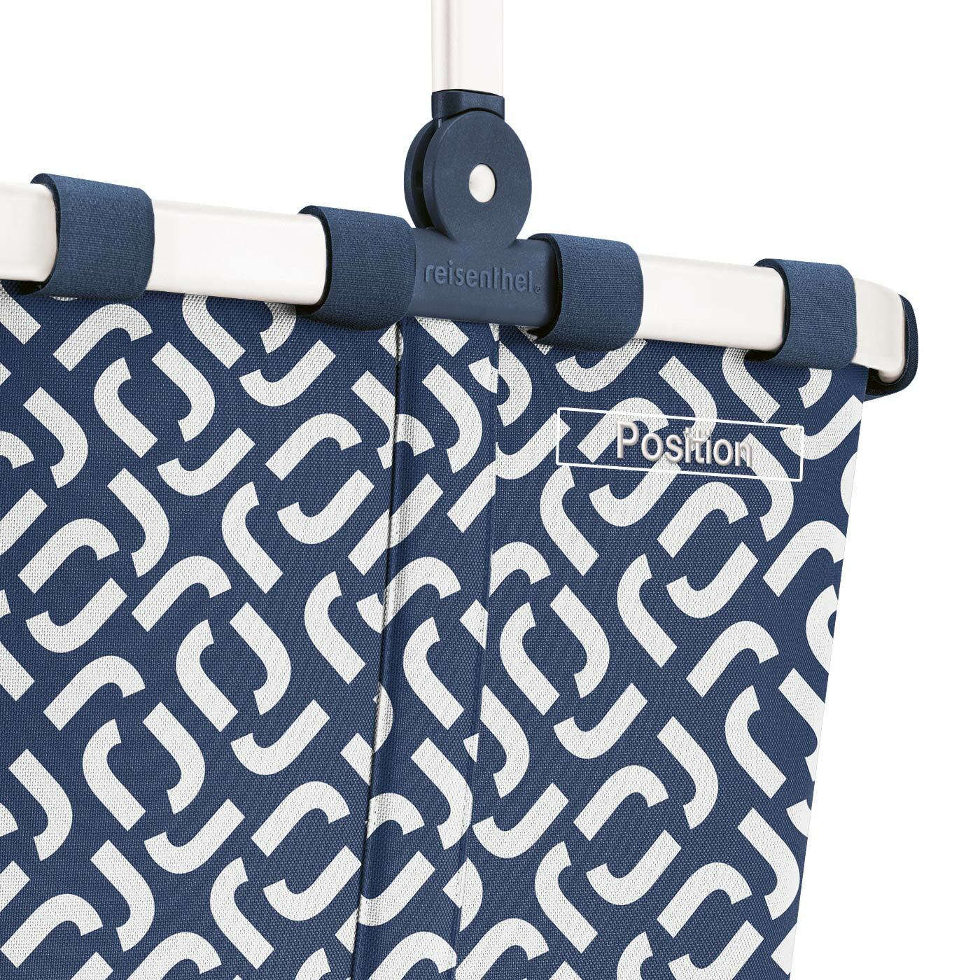 Nahaufnahme eines blauen Einkaufskorbs mit weißem geometrischem Muster und einem stabilen weißen Rahmen, seitliche Perspektive.