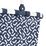 Close-up van een blauwe boodschappenmand met een wit geometrisch patroon en een stevig wit frame, gezien vanuit de zijkant.